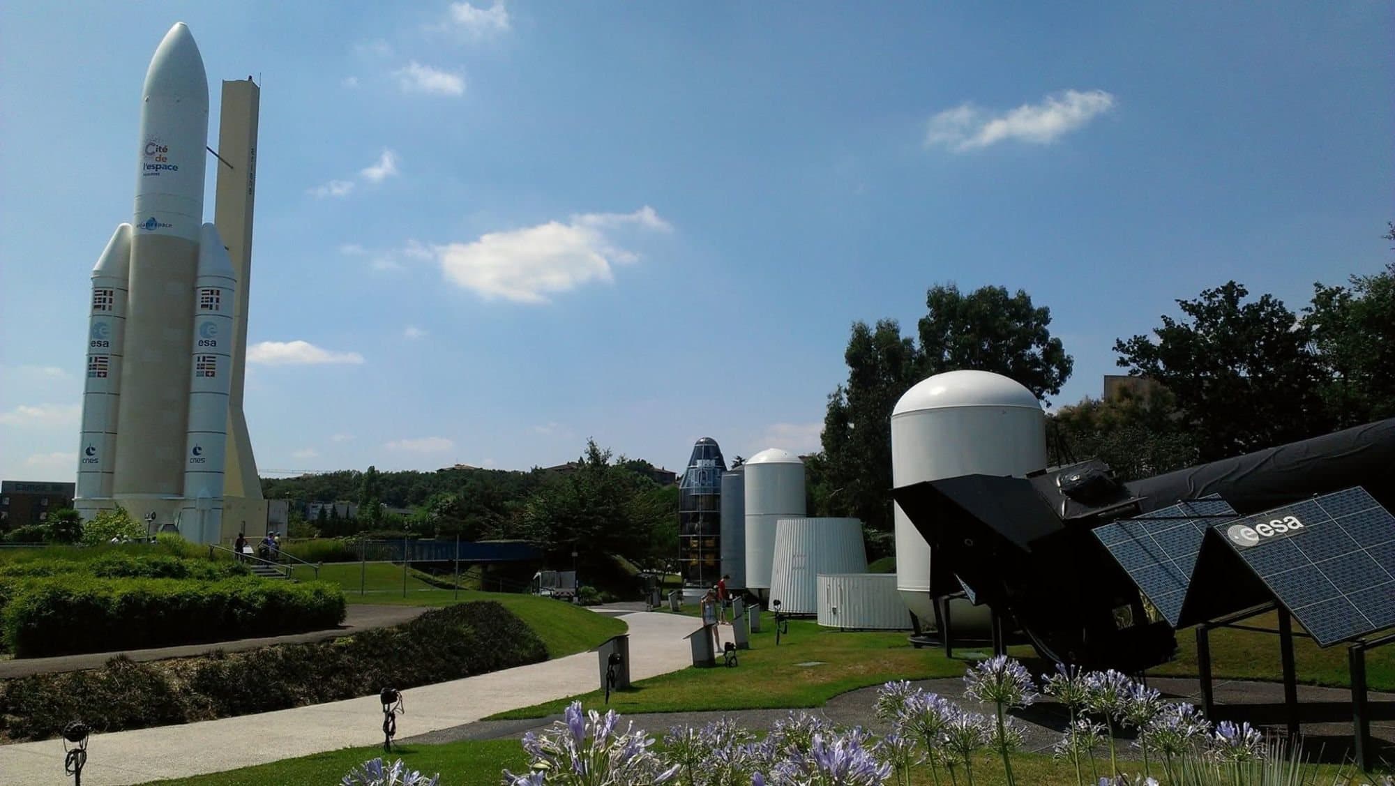 An Ariane 5 replica, rocket stage exhibits and a spacecraft model in a garden