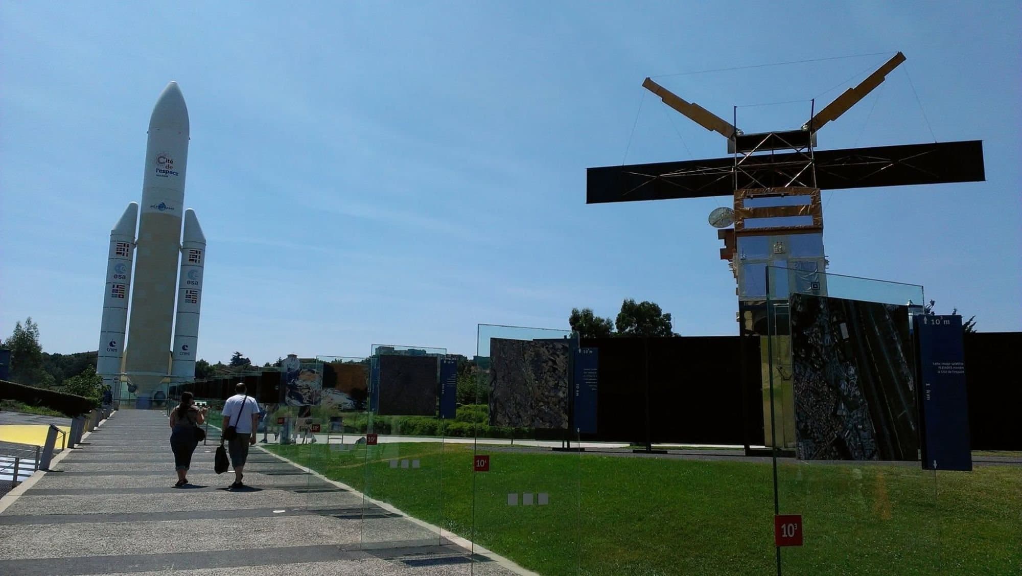 A walkway leading to an Ariane 5 replica, with an Earth-observation satellite model on the right