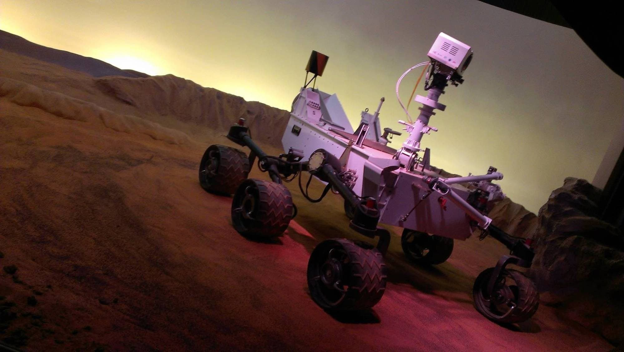 A model of the Curiosity Mars rover on a simulated Martian surface in warm light