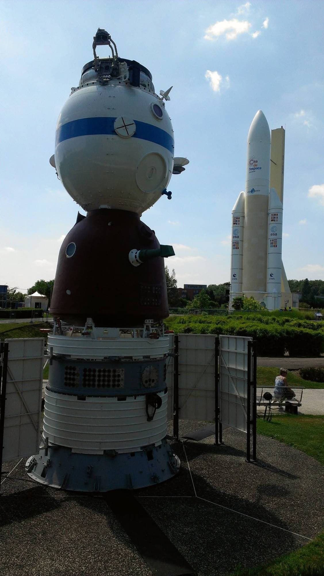 A backlit Soyuz spacecraft exhibit with an Ariane 5 replica standing in the distance