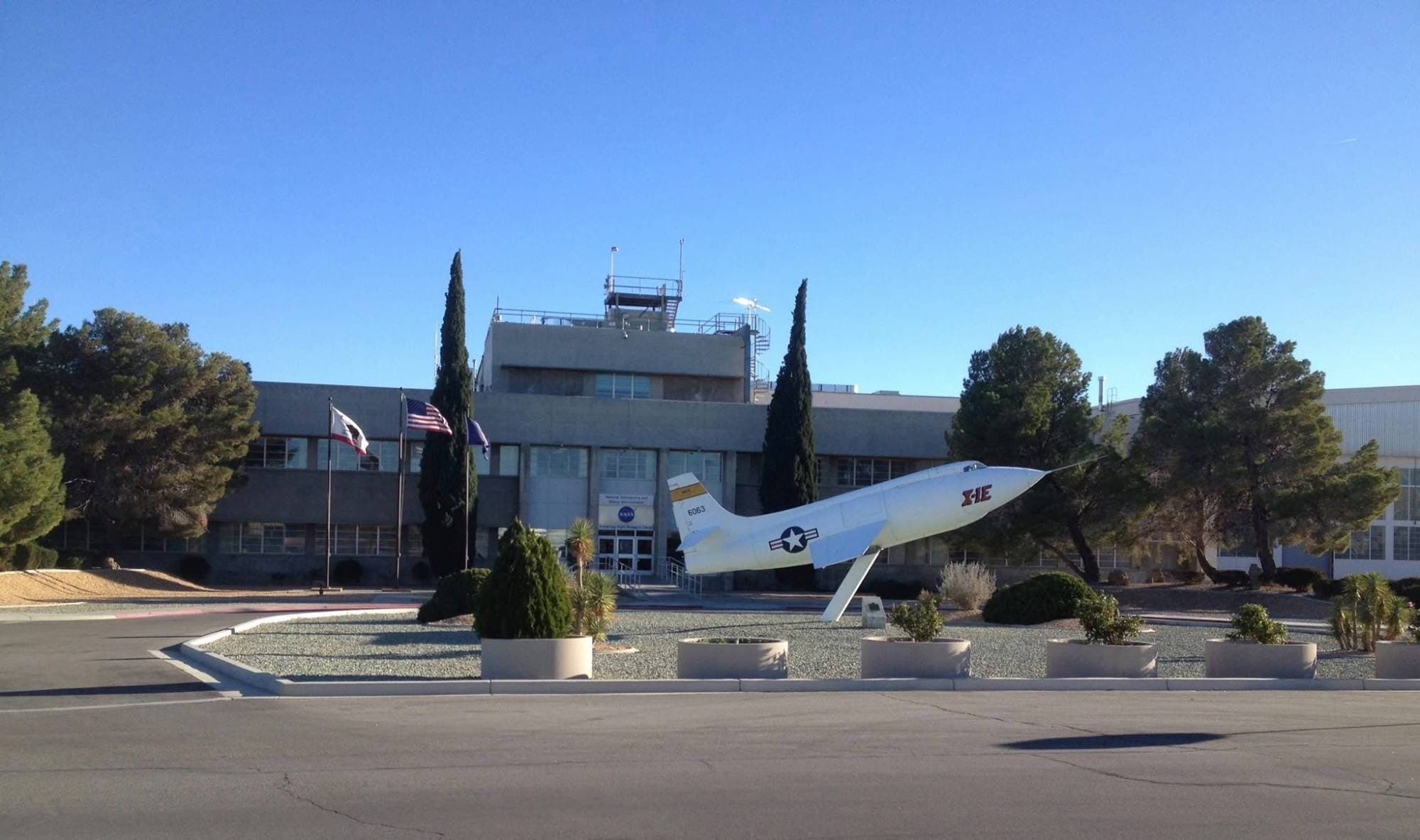 The X-1E research aircraft mounted nose-up in front of a flight research headquarters building