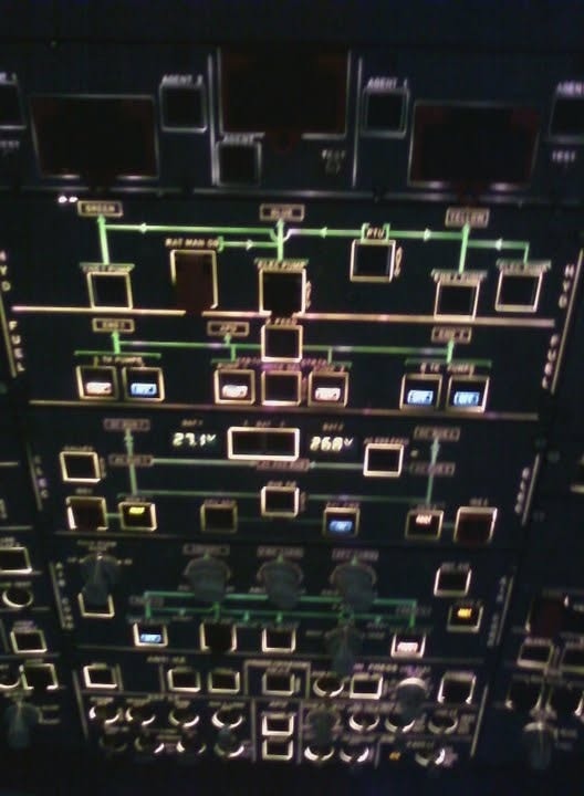 An A320 overhead panel at night with illuminated hydraulic, fuel and electrical system lines