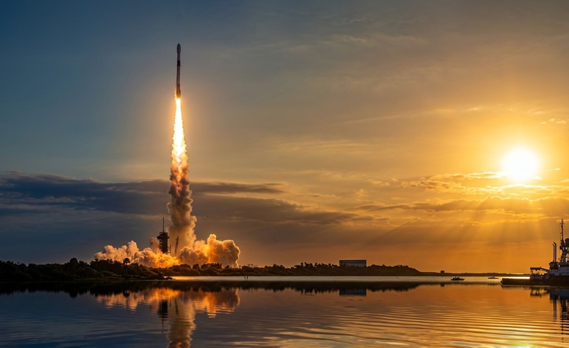 A launch vehicle climbing on a column of flame at sunset, its exhaust cloud reflected in the water