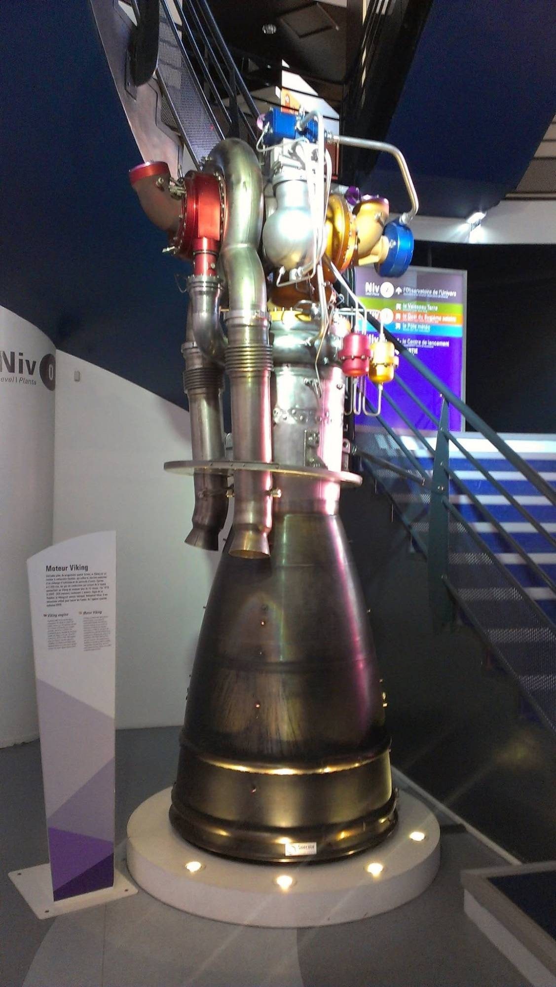 A Viking liquid-fuel rocket engine with its turbopump and bronze nozzle on a lit plinth